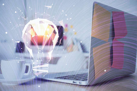 Computer on desktop in office with bulb icon hologram. Double exposure. Concept of idea.