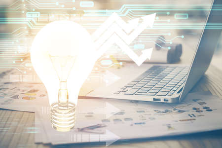 Computer on desktop in office with bulb icon hologram. Multi exposure. Concept of idea.