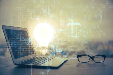 Computer on desktop in office with bulb icon hologram. Multi exposure. Concept of idea.の写真素材