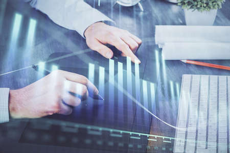 Double exposure of man's hands holding and using a phone and financial graph drawing. Analysis...