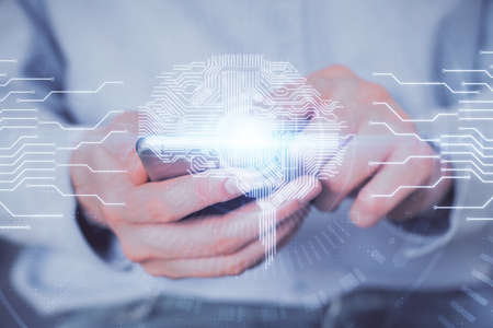 Double exposure of man's hand holding and using a digital device and brain hologram drawing. Data...