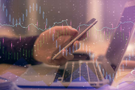 Double exposure of man's hands holding and using a phone and financial graph drawing. Analysis...