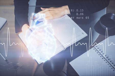 Heart hologram over woman's hands writing background. Concept of Medical study. Multi exposureの写真素材