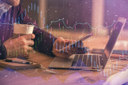 Double exposure of man's hands holding and using a phone and financial graph drawing. Analysis...