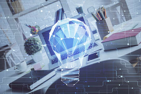 Computer on desktop in office with bulb icon hologram. Double exposure. Concept of idea.の写真素材