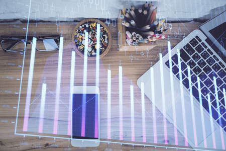Double exposure of financial graph hologram over desktop with phone. Top view. Mobile trade platform concept.の写真素材