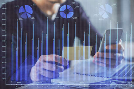 Double exposure of man's hands holding and using a phone and financial graph drawing. Analysis...