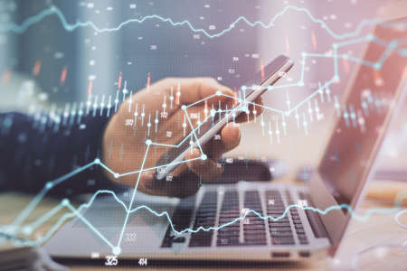 Double exposure of man's hands holding and using a phone and financial graph drawing. Analysis...