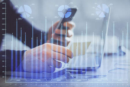 Double exposure of man's hands holding and using a phone and financial graph drawing. Analysis...