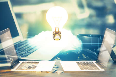 Computer on desktop in office with bulb icon hologram. Multi exposure. Concept of idea.