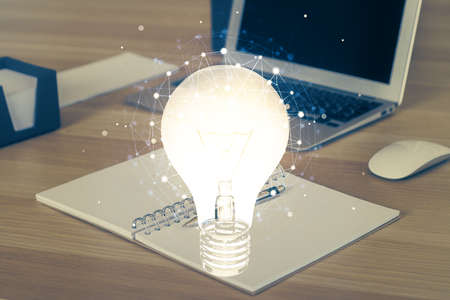 Computer on desktop in office with bulb icon hologram. Multi exposure. Concept of idea.の写真素材