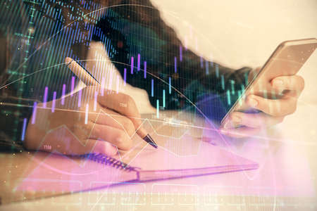 Double exposure of forex graph sketch hologram and woman holding and using a mobile device. Stock...