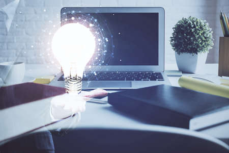 Computer on desktop in office with bulb icon hologram. Double exposure. Concept of idea.