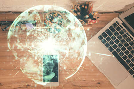 Double exposure of business theme hologram over desktop with phone. Top view. Mobile international...