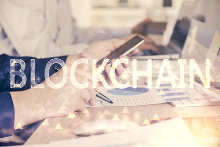 Double exposure of mans hands holding and using a phone and crypto currency blockchain theme...