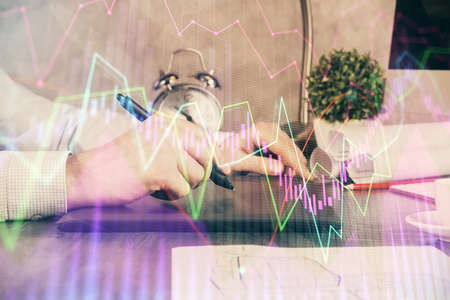 Double exposure of mans hands holding and using a phone and financial graph drawing. Analysis...