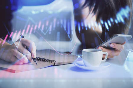 Double exposure of forex graph sketch hologram and woman holding and using a mobile device. Stock...