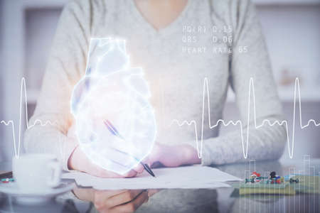 Heart hologram over womans hands writing background. Concept of Medical study. Multi exposureの写真素材