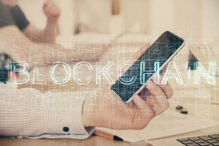 Double exposure of mans hands holding and using a phone and crypto currency blockchain theme...