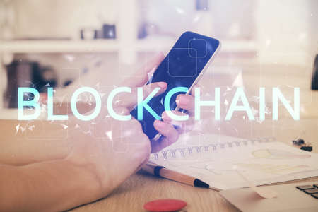Double exposure of mans hands holding and using a phone and crypto currency blockchain theme...