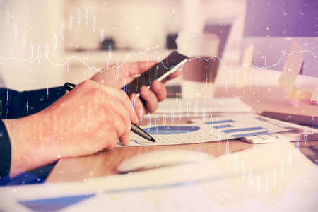 Double exposure of mans hands holding and using a phone and financial graph drawing. Analysis...