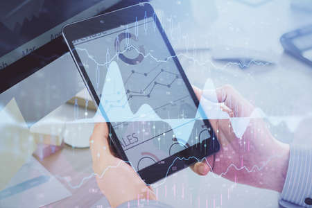 Double exposure of mans hands holding and using a phone and financial graph drawing. Analysis...