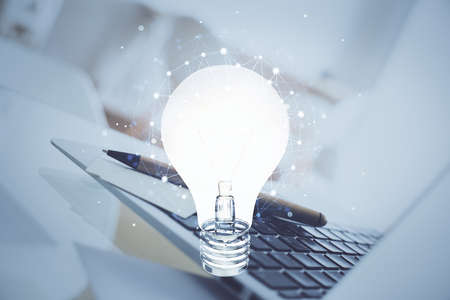 Computer on desktop in office with bulb icon hologram. Double exposure. Concept of idea.の写真素材
