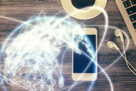 Double exposure of business theme hologram over desktop with phone. Top view. Mobile international...