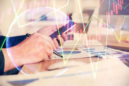 Double exposure of mans hands holding and using a phone and financial graph drawing. Analysis...