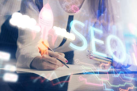 Double exposure of womans hands making notes with SEO icon. Concept of Search engine optimizationの写真素材