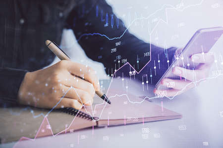 Double exposure of forex graph sketch hologram and woman holding and using a mobile device. Stock...