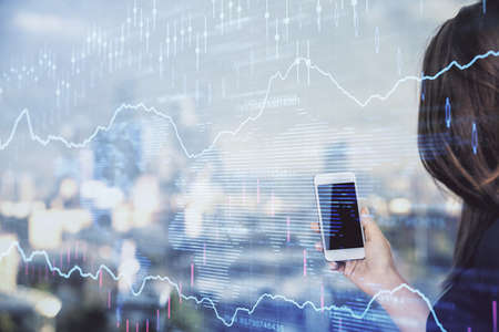 Double exposure of forex chart sketch hologram and woman holding and using a mobile device. Stock...