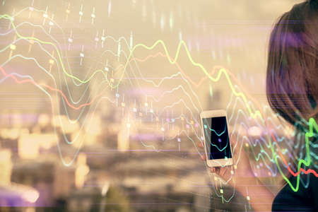 Double exposure of forex chart sketch hologram and woman holding and using a mobile device. Stock market concept.の写真素材