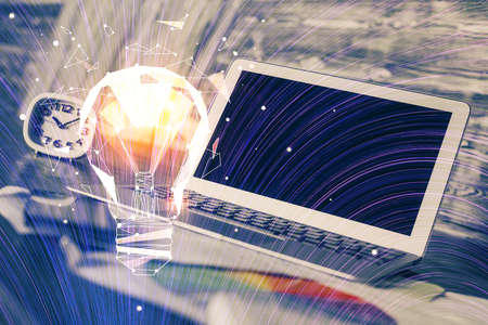 Computer on desktop in office with bulb icon hologram. Multi exposure. Concept of idea.