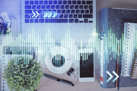 Double exposure of financial graph hologram over desktop with phone. Top view. Mobile trade platform...
