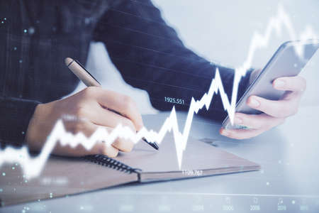 Double exposure of forex graph sketch hologram and woman holding and using a mobile device. Stock...