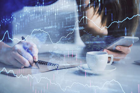 Double exposure of forex graph sketch hologram and woman holding and using a mobile device. Stock...