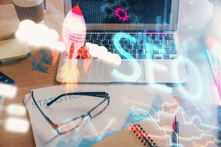 Double exposure of table with computer and seo drawing hologram. Search optimization concept.