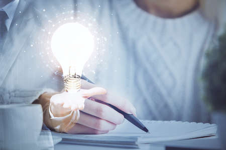 Drawing bulb over womans hands taking notes background. Concept of idea. Double exposureの写真素材