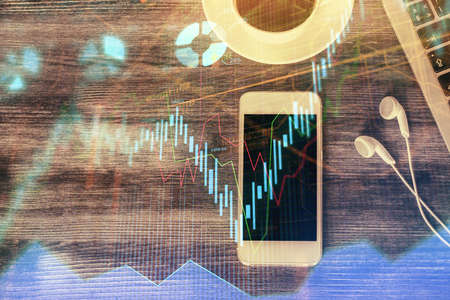 Double exposure of forex chart hologram over desktop with phone. Top view. Mobile trade platform concept.の写真素材