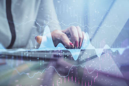 Double exposure of businesswoman hands typing on computer and financial graph hologram drawing....