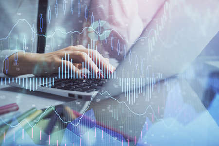 Double exposure of woman hands typing on computer and financial graph hologram drawing. Stock market...