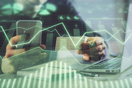 Double exposure of mans hands holding and using a phone and financial graph drawing. Analysis...