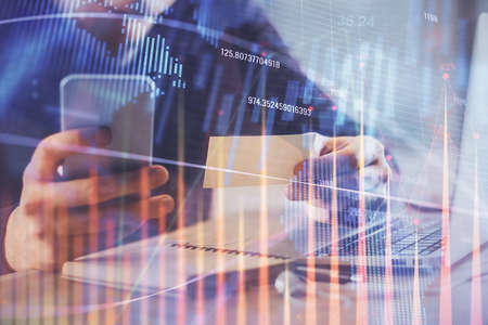 Double exposure of mans hands holding and using a phone and financial graph drawing. Analysis...