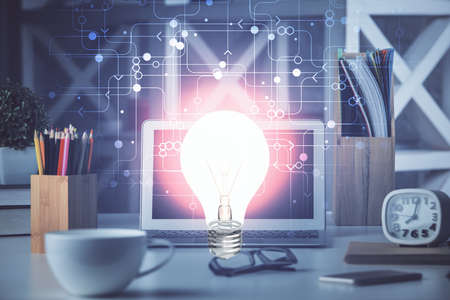 Computer on desktop in office with bulb icon hologram. Double exposure. Concept of idea.の写真素材
