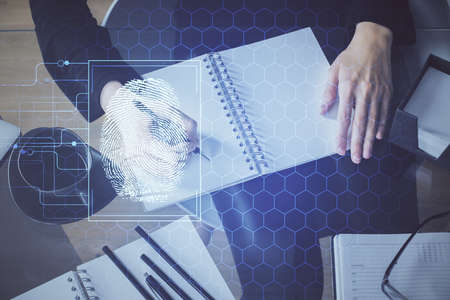 Blue fingerprint hologram over hands taking notes background. Concept of security. Double exposure