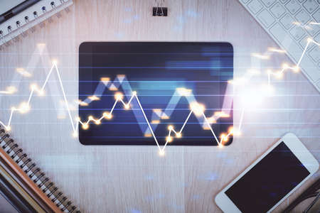 Double exposure of forex graph hologram over desktop with phone. Top view. Mobile trade platform...