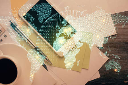 Double exposure of business theme hologram over desktop with phone. Top view. Mobile international trade connection concept.の写真素材