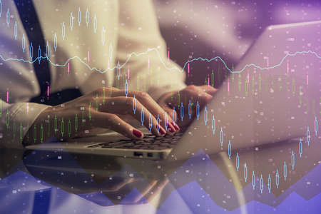Double exposure of businesswoman hands typing on computer and financial graph hologram drawing....