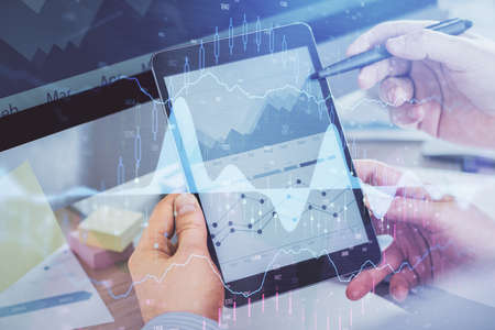 Double exposure of mans hands holding and using a phone and financial chart drawing. Market analysis...
